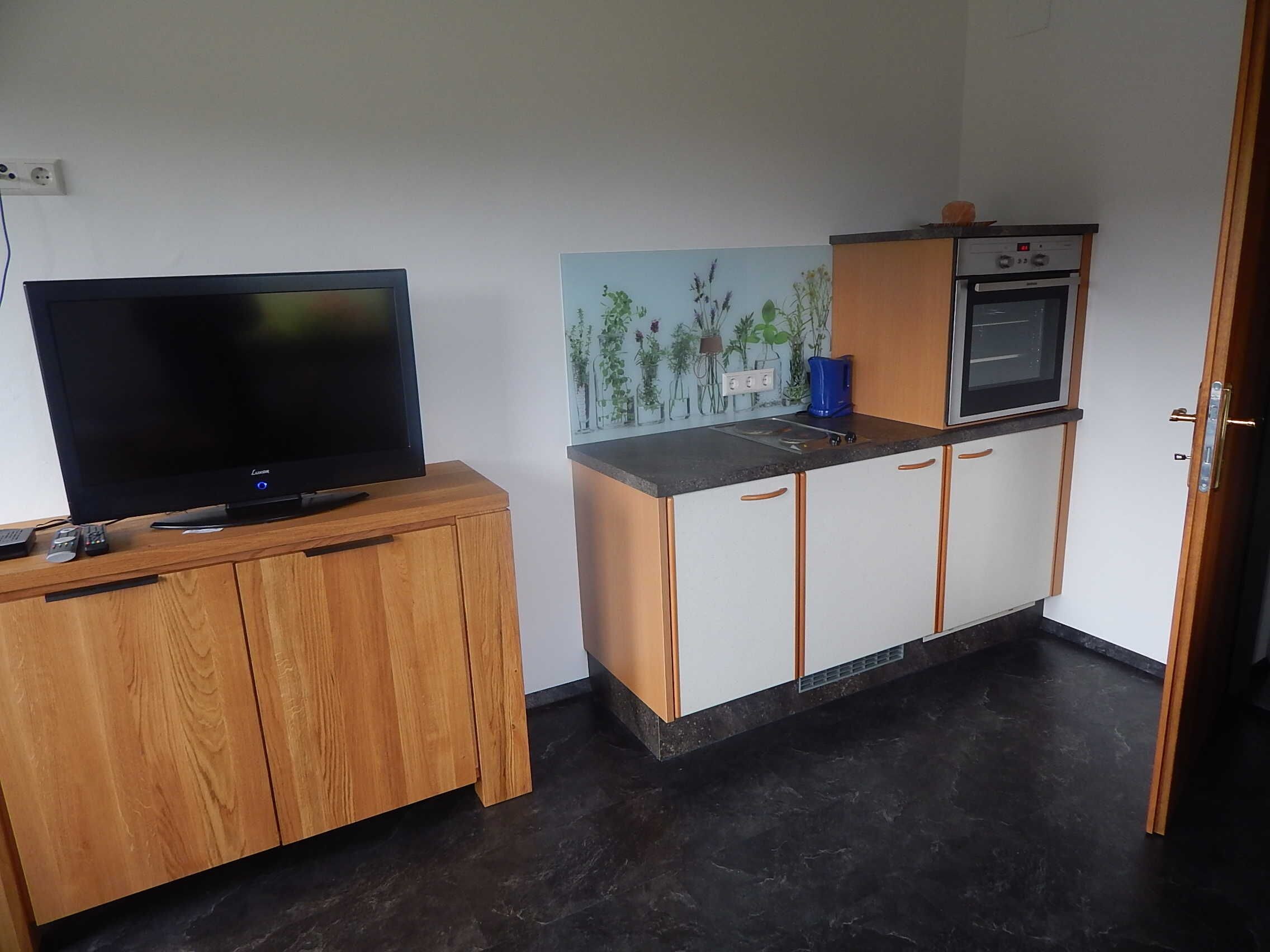 Eine kleine Küchenzeile mit Fernseher, Kaffeemaschine und Backofen.