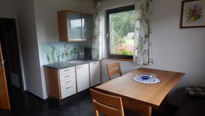 Una cocina compacta con comedor, una ventana con cortinas y vistas al exterior con vegetación.