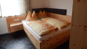Una cama de madera con cabecera, una mesita de noche, una ventana con cortinas y un piso negro.