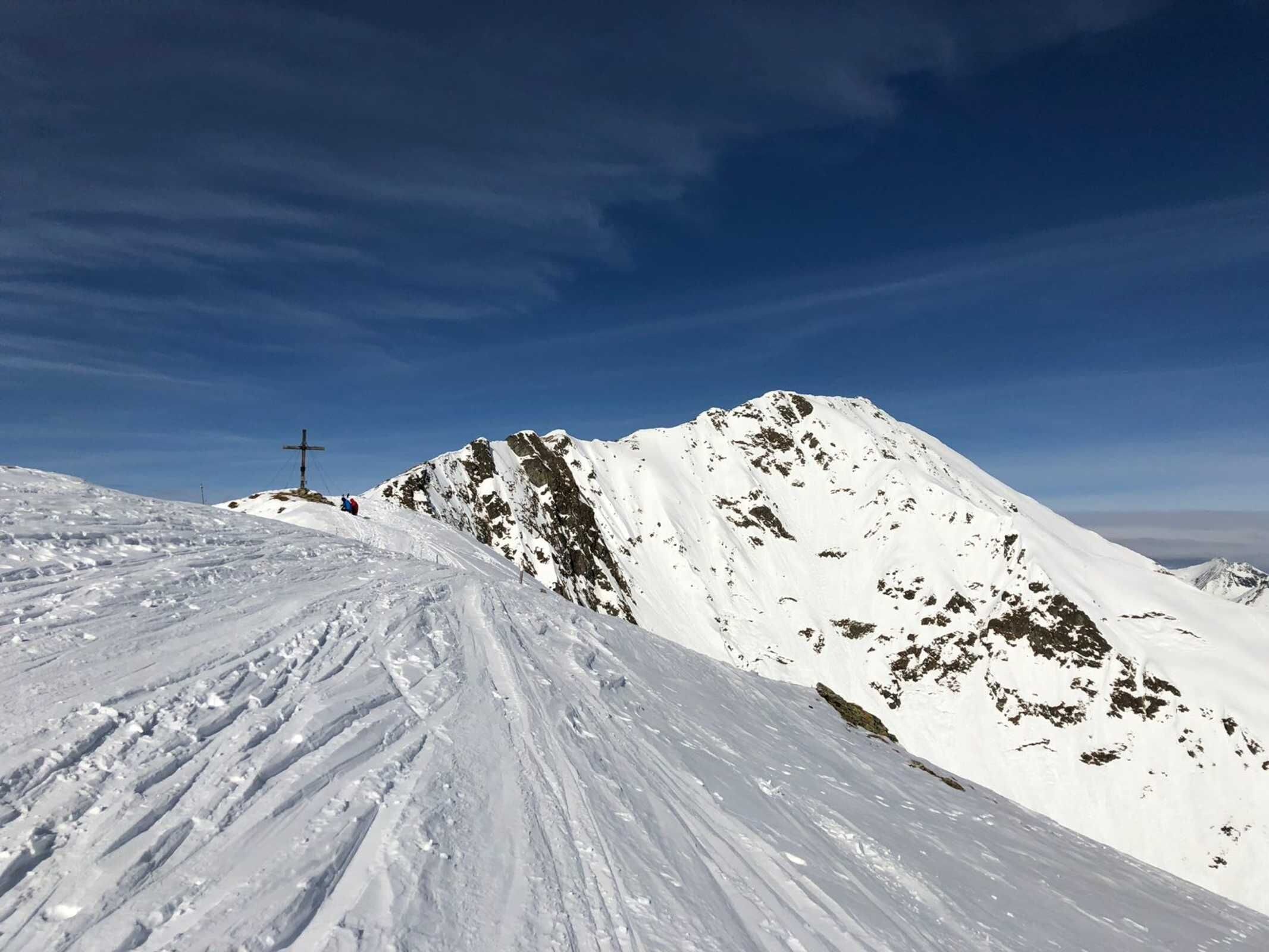 Ein mit Schnee bedeckter Berghang, in der Ferne eine Kreuzkonstruktion.