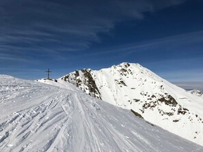 Pendiente nevada de una montaña con una estructura cruciforme a lo lejos.