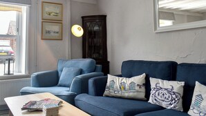 Ein Wohnzimmer mit blauem Sofagarnitur, einem Holztisch und gerahmten Bildern an der Wand.