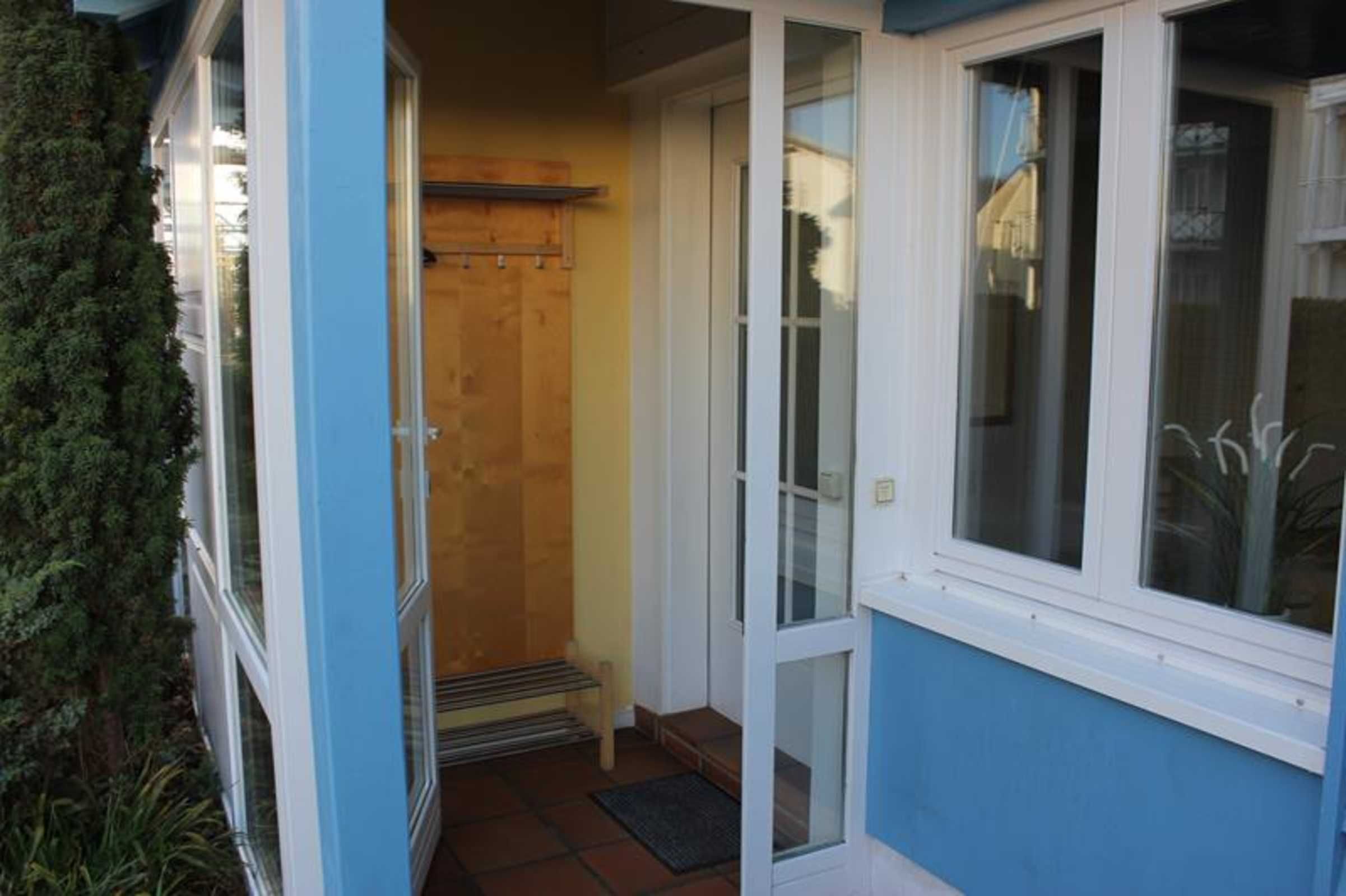 Exterior azul com porta de vidro e janelas, porta de madeira e um pequeno degrau que leva à entrada.