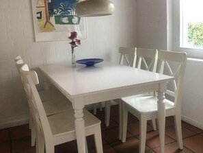 Una mesa de comedor blanca con seis sillas, un cuenco azul y un florero con flores.