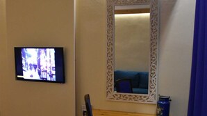 Habitació amb televisió penjada a la paret, taula de fusta amb una cadira i un mirall decoratiu.