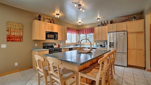 A modern kitchen with wooden cabinets, a central island with chairs, a refrigerator, and a microwave. - Secluded mountain retreat (Dolores)