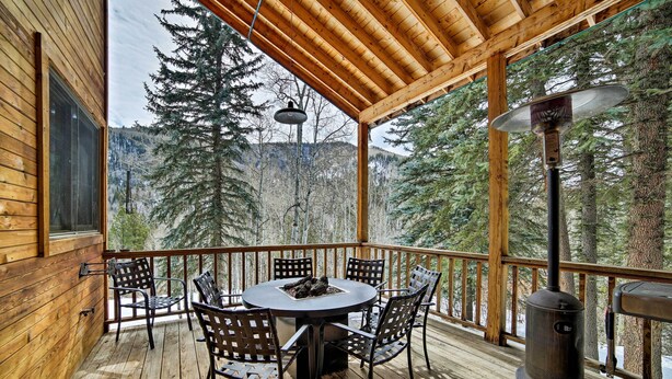 A wooden deck with a round table and chairs, a heater, and a view of a forested mountain. - Secluded mountain retreat (Dolores)