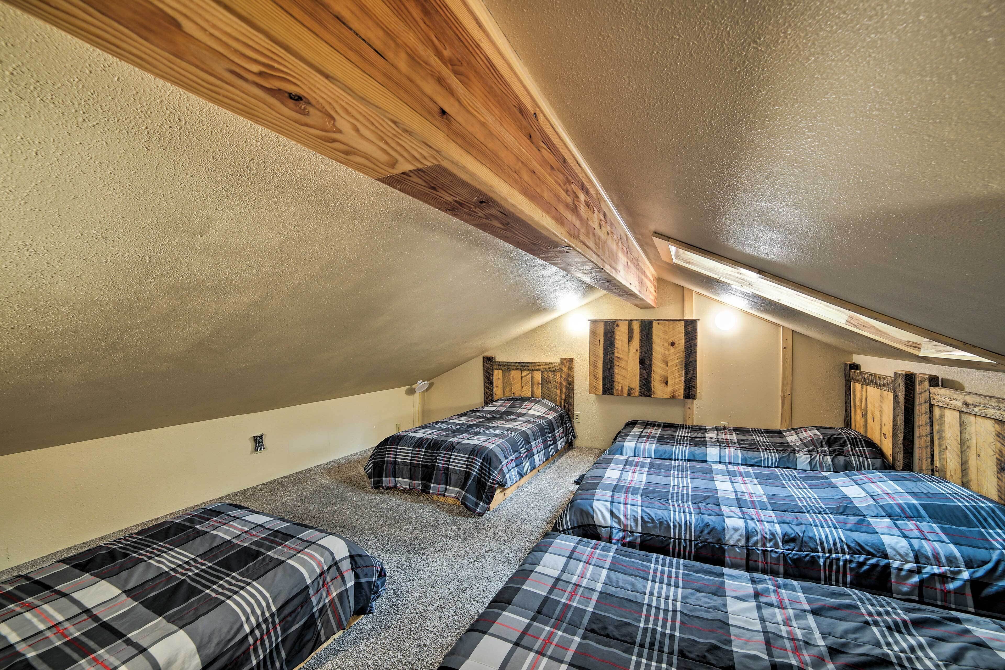A dormitory room with three beds, wooden beams on the ceiling, and a sloped ceiling.