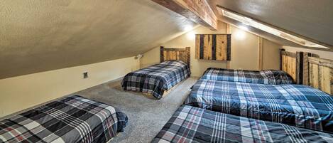 A dormitory room with three beds, wooden beams on the ceiling, and a sloped ceiling.