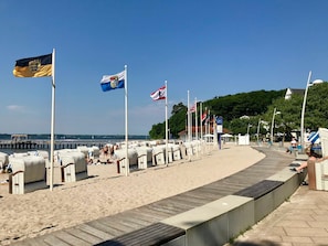 Une promenade en bord de mer, avec des drapeaux, des chaises de plage et une jetée en arrière-plan.