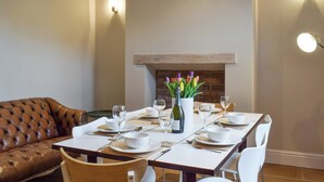 A dining area with a long table set for four, a brown leather couch, and a brick fireplace. - 3 bedroom accommodation in Skipton (Skipton)