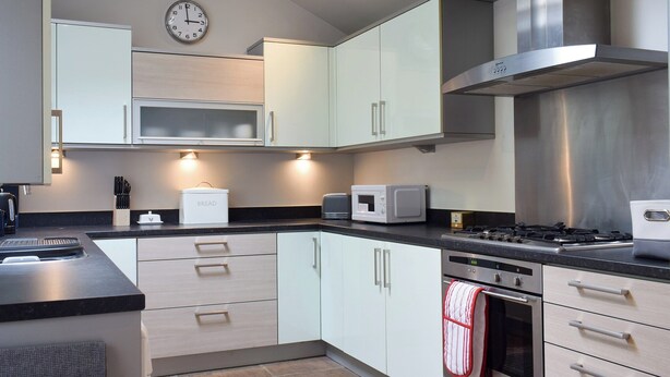 A modern kitchen with white cabinets, a stainless steel range hood, a microwave, and a bread box. - 3 bedroom accommodation in Skipton (Skipton)