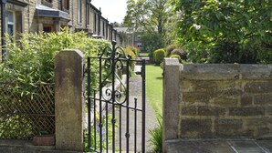 A stone gate with a wrought iron design, leading to a well-maintained lawn and a row of terraced houses. - 3 bedroom accommodation in Skipton (Skipton)