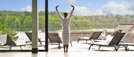 A person in a white robe standing by a pool with a view of a forested hill.