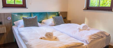Un lit double avec du linge de lit blanc et deux serviettes enroulées, une tête de lit de couleur turquoise et deux tables de chevet avec des lampes.
