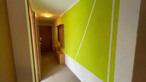 A narrow hallway with a door at the end, a wooden bench, and a wall with a geometric pattern. - 08 DZ - Island-Hotel Dobbertin (Dobbertin)