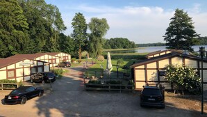 A hotel with a gravel driveway, parked cars, and a view of a lake. - 08 DZ - Island-Hotel Dobbertin (Dobbertin)