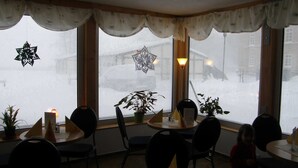 A restaurant with round tables and chairs, potted plants, and a view of a snowy street through the windows. - 08 DZ - Island-Hotel Dobbertin (Dobbertin)