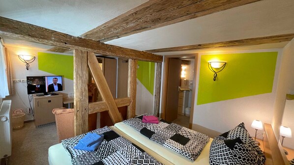 Una habitación con techo de madera, cama con ropa de cama estampada, escritorio con ordenador y pared verde.