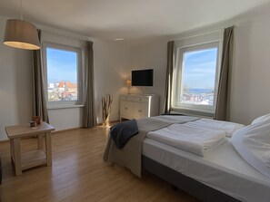 A hotel room with a bed, bedside table, lamp, TV, and large windows with curtains.