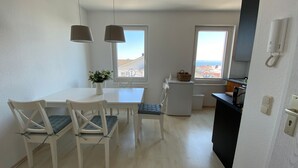 Una cocina moderna con electrodomésticos blancos, un comedor con mesa y sillas, y ventanas amplias con vistas.