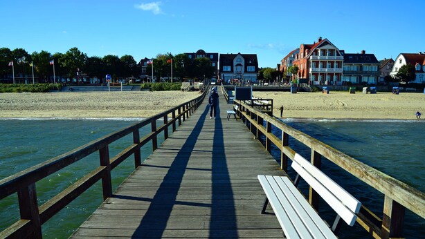 Un muelle de madera que conduce a una playa, con edificios al fondo.