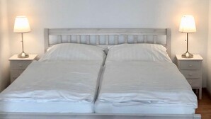Una cama doble con ropa de cama blanca, dos mesitas de noche con lámparas y un cabecero de madera.