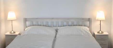Una cama doble con ropa de cama blanca, dos mesitas de noche con lámparas y un cabecero de madera.
