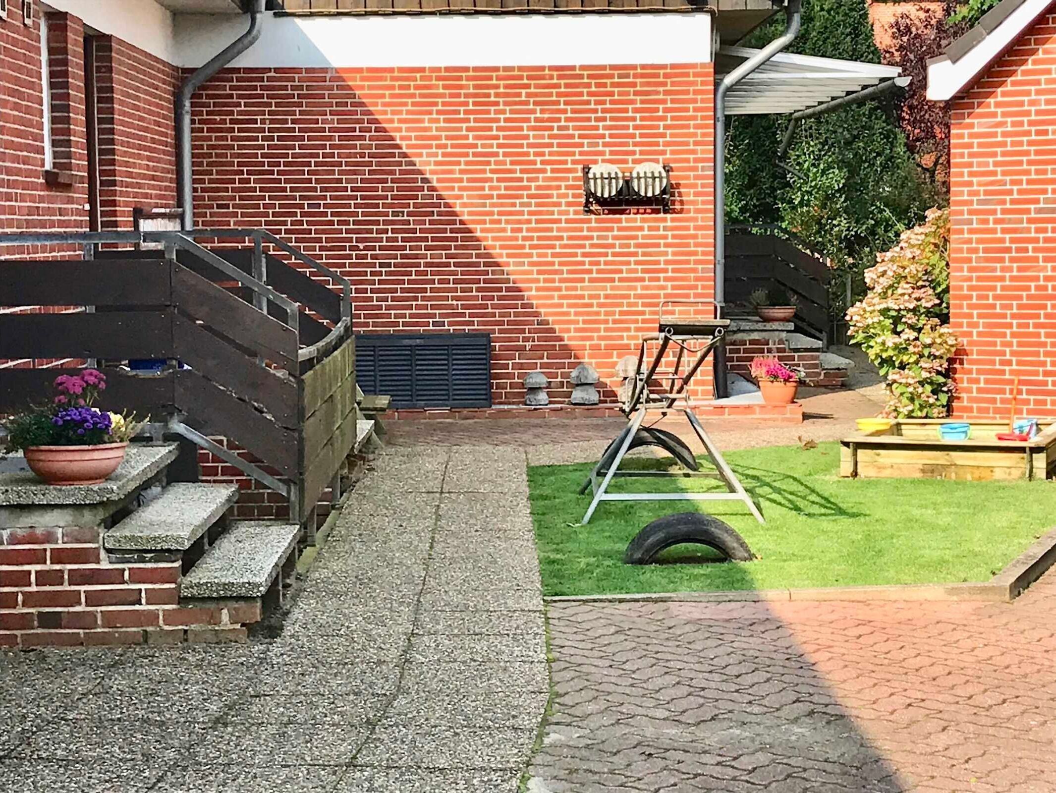 Un patio de ladrillo con un pequeño césped, una silla metálica y un columpio hecho con neumático.