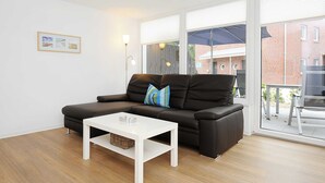 A modern living room with a black leather sofa, a white coffee table, and a framed picture on the wall. - Vacation apartment Leuchtturm - Haus Kunterbunt (Esens)