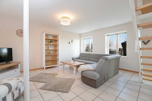 A modern living room with a grey sofa, a wooden coffee table, a bookshelf, and a television.