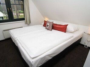 A single bed with white bedding, a brown pillow, and a red pillow. There is a window with a view of trees and a building outside. - 95m² holiday home - holiday homes on the lake (Nossentiner Hütte)