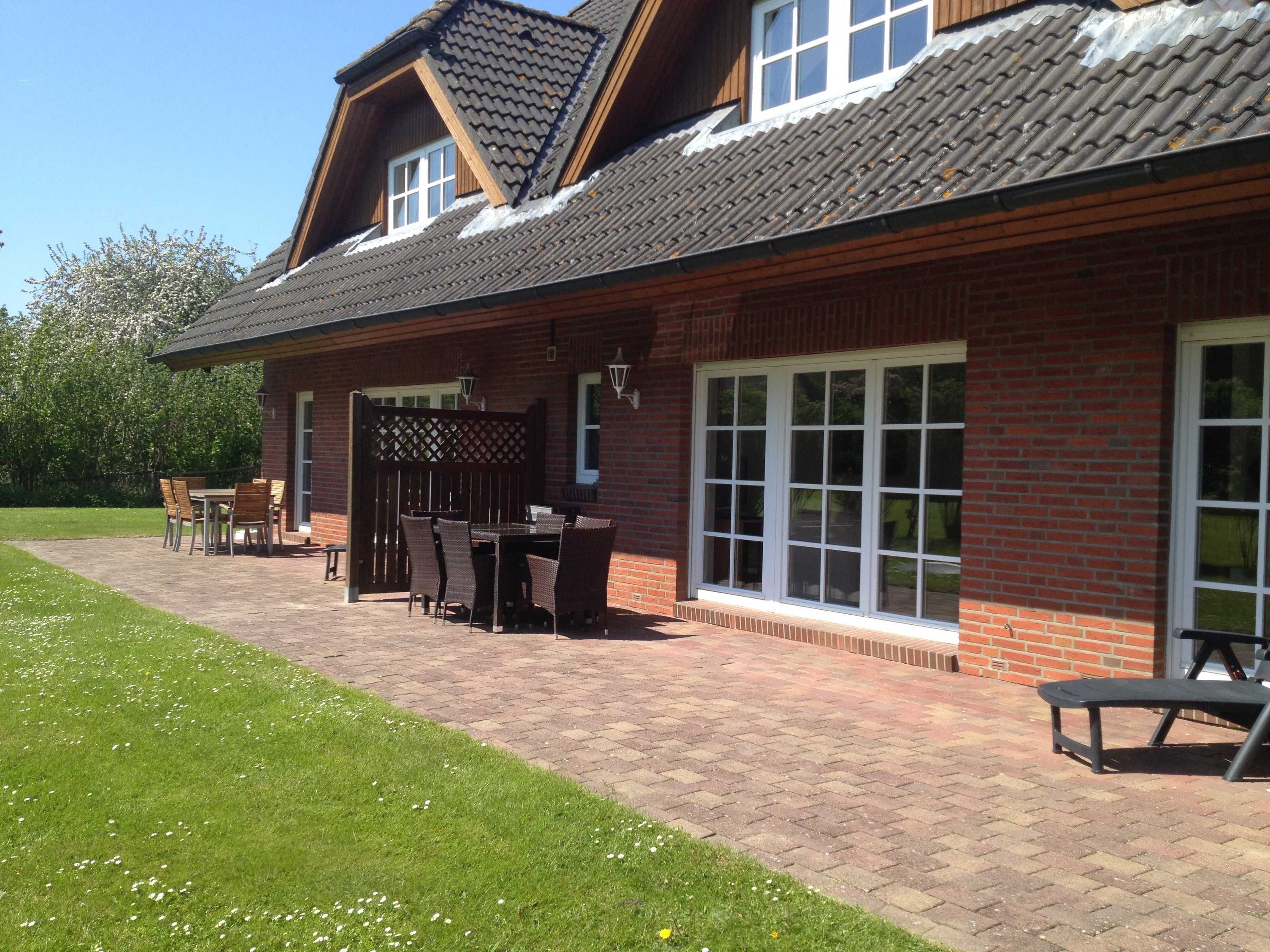 A two-story house with a brick exterior, large windows, and a patio with outdoor furniture.