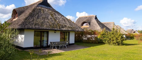 Una casa moderna con techo de paja, un patio con mobiliario exterior y un césped cuidado.