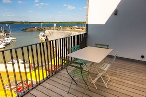 A balcony with a table and chairs, overlooking a marina with boats and a beach. - The Edged (06) - Z1-THE HOUSE (Zwenkau)