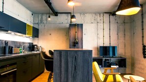 A modern kitchen with dark cabinets, a central island, and a dining area with a TV and sound system. - The Edged (06) - Z1-THE HOUSE (Zwenkau)