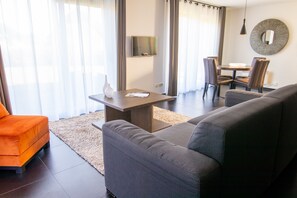 A modern living room with a sofa, a dining table, and a TV mounted on the wall.