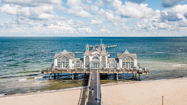 Ein Hotel am Wasser mit einer Anlegestelle, die sich ins Meer erstreckt, mit mehreren Gebäuden und großen Fenstern sowie einem zentralen Turm.