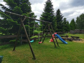 A wooden swing set and a slide in a grassy outdoor area with trees in the background. - Sleeping in the hay / hay bed - Ferienhof Sarodnick (Lauta)
