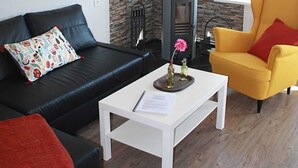 Una sala de estar con una pared de piedra, un sofá de cuero negro, una mesa de centro blanca y un sillón amarillo.