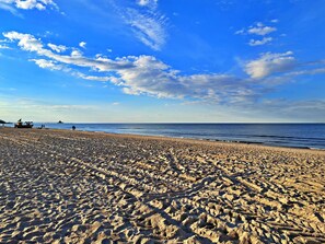A beach with a clear sky, a boat, and a pier in the distance.