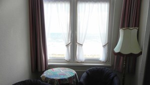 Ein Zimmer mit zwei Sesseln, einem kleinen Tisch und Meerblick durch transparente Vorhänge.