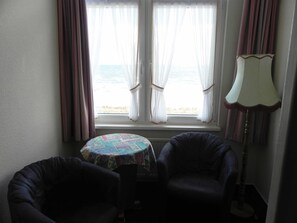 Une pièce avec deux chaises, une petite table et une vue sur la mer, visible à travers de fines rideaux.