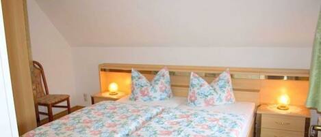 Een slaapkamer met een houten bed, bloemenbeddengoed, twee nachtkastjes met lampen, en een stoel.