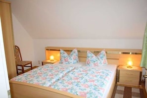 A bedroom with a wooden bed, floral bedding, two bedside tables with lamps, and a chair. - App 1 (40m²) - Rügen-Fewo 267 (Mönchgut)