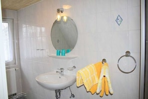 A bathroom with a white sink, a round mirror, and a towel rack with towels. - App 1 (40m²) - Rügen-Fewo 267 (Mönchgut)