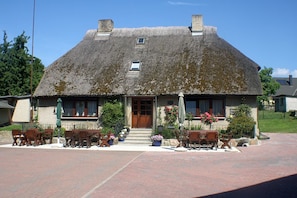 A traditional building with a thatched roof, a wooden door, and a small window. There are outdoor seating arrangements and potted plants. - App 1 (40m²) - Rügen-Fewo 267 (Mönchgut)