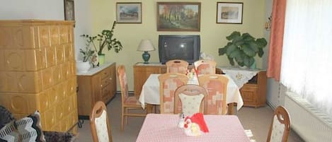 Ein Essbereich mit kariertem Tischläufer, Holzsesseln, einem Fernseher und gerahmten Bildern an der Wand.