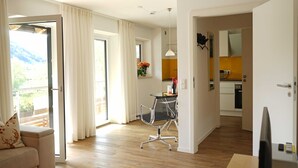 Ein großzügiger Wohnbereich mit Sofa, Esstisch, einer Küche im Hintergrund und einem Balkon mit Vorhängen.
