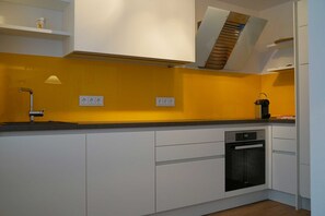 Une cuisine avec des armoires blanches, un four encastré et un pare-feu jaune.